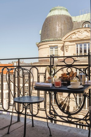 A balcony with a table set for breakfast, including bread, eggs, and beverages, overlooking a historic building with a dome. - Hotel Montalembert (Paris)