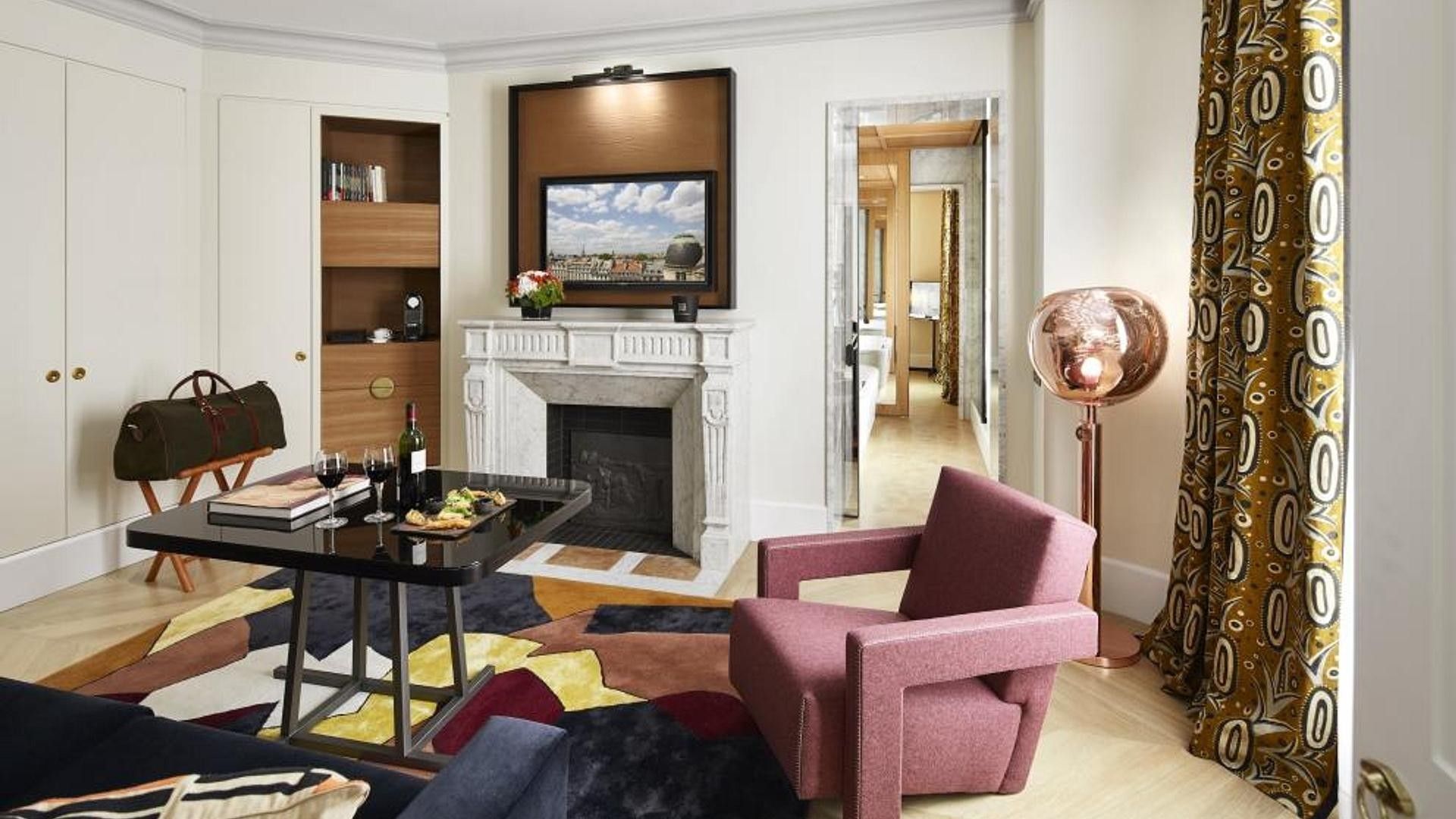 A living room with a fireplace, a television mounted above it, and a dining area with a table set for two.