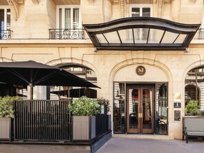 A hotel entrance with a classic facade, a covered entrance, and outdoor seating with umbrellas. - Hotel Montalembert (Paris)