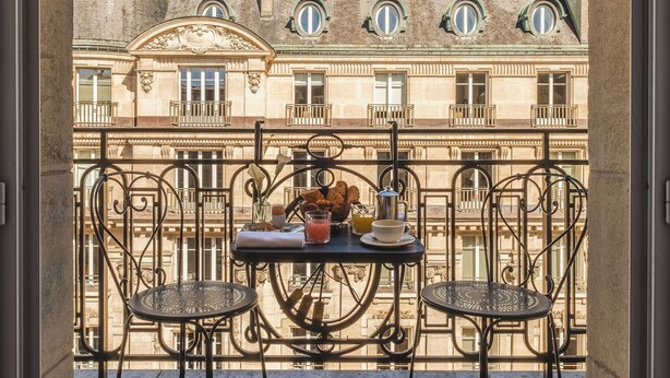 A balcony with a table and chairs, a view of a historic building with multiple windows and balconies. - Hotel Montalembert (Paris)
