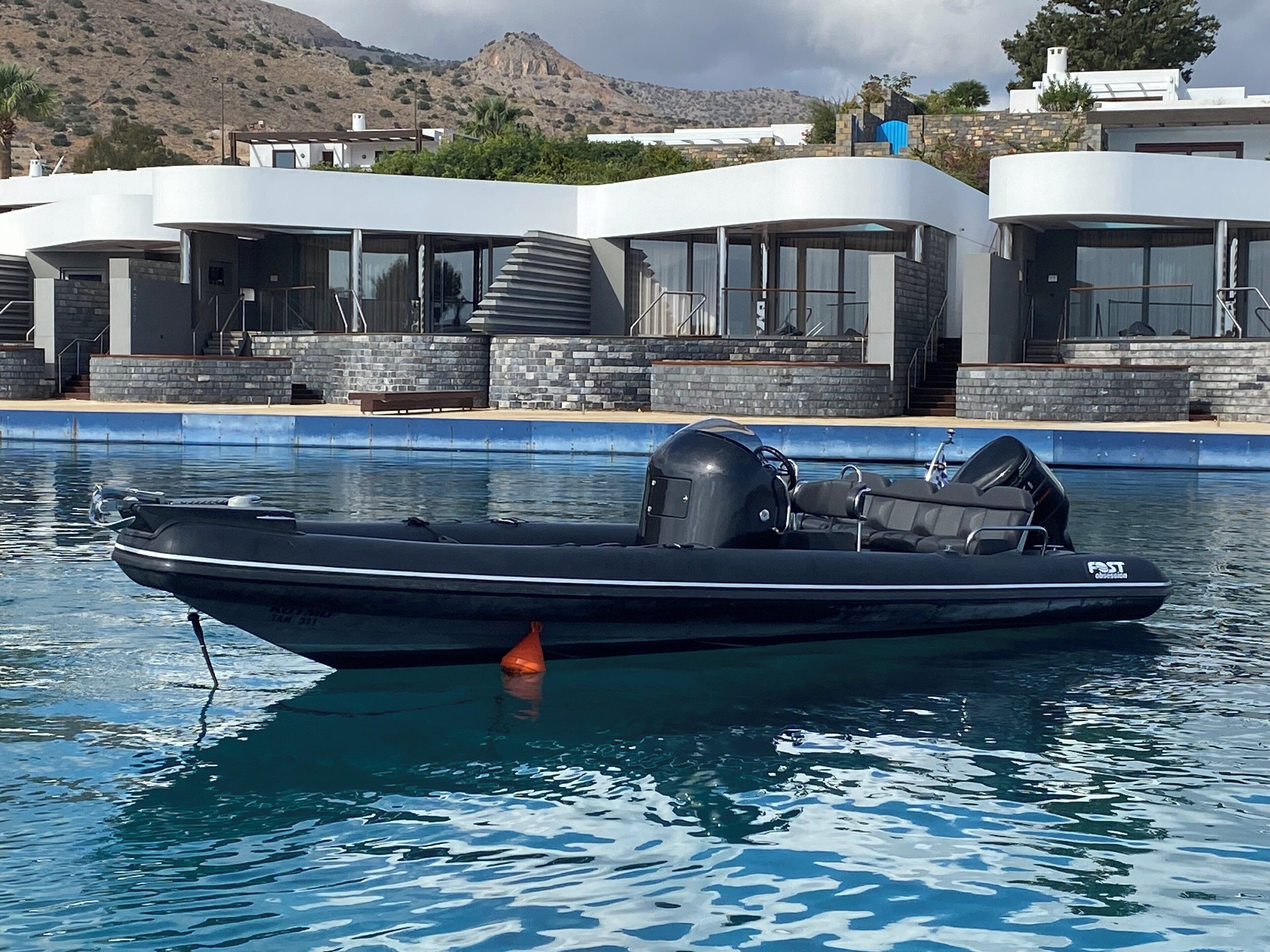 A modern boat docked at a pool with a mountainous backdrop.