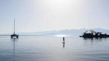 Um lago tranquilo com um veleiro e uma pessoa praticando stand-up paddle.