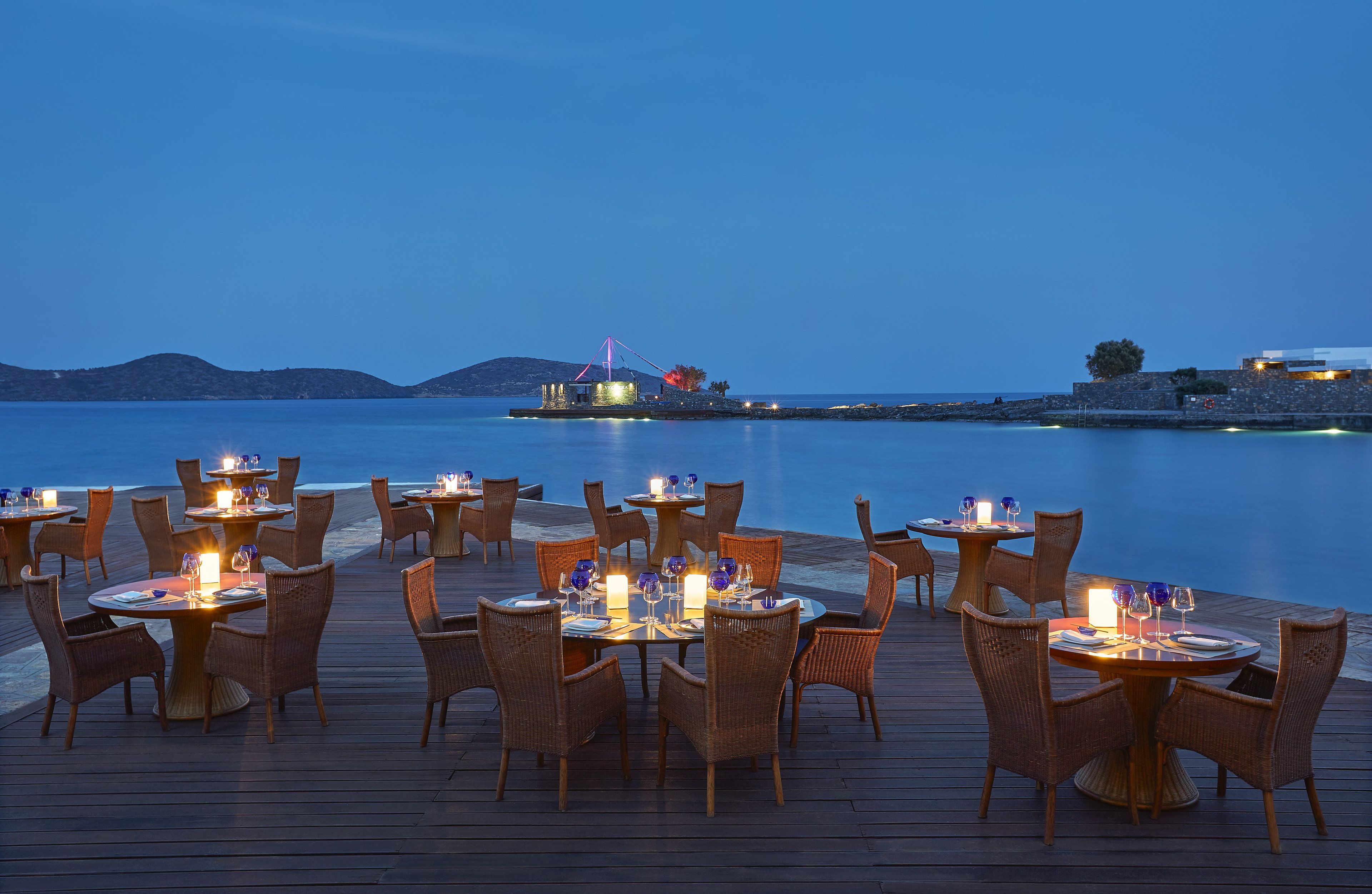 Un comedor junto al agua, con mesas preparadas para la cena y vistas al mar.
