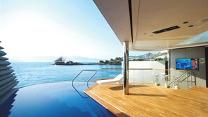 Cubierta de un lujoso yate con piscina, pantalla de televisión y vistas al mar y a la costa lejana.