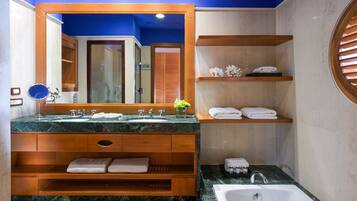 Un baño moderno con un espejo grande, encimeras de mármol, tocador de madera, repisas con toallas y una bañera.