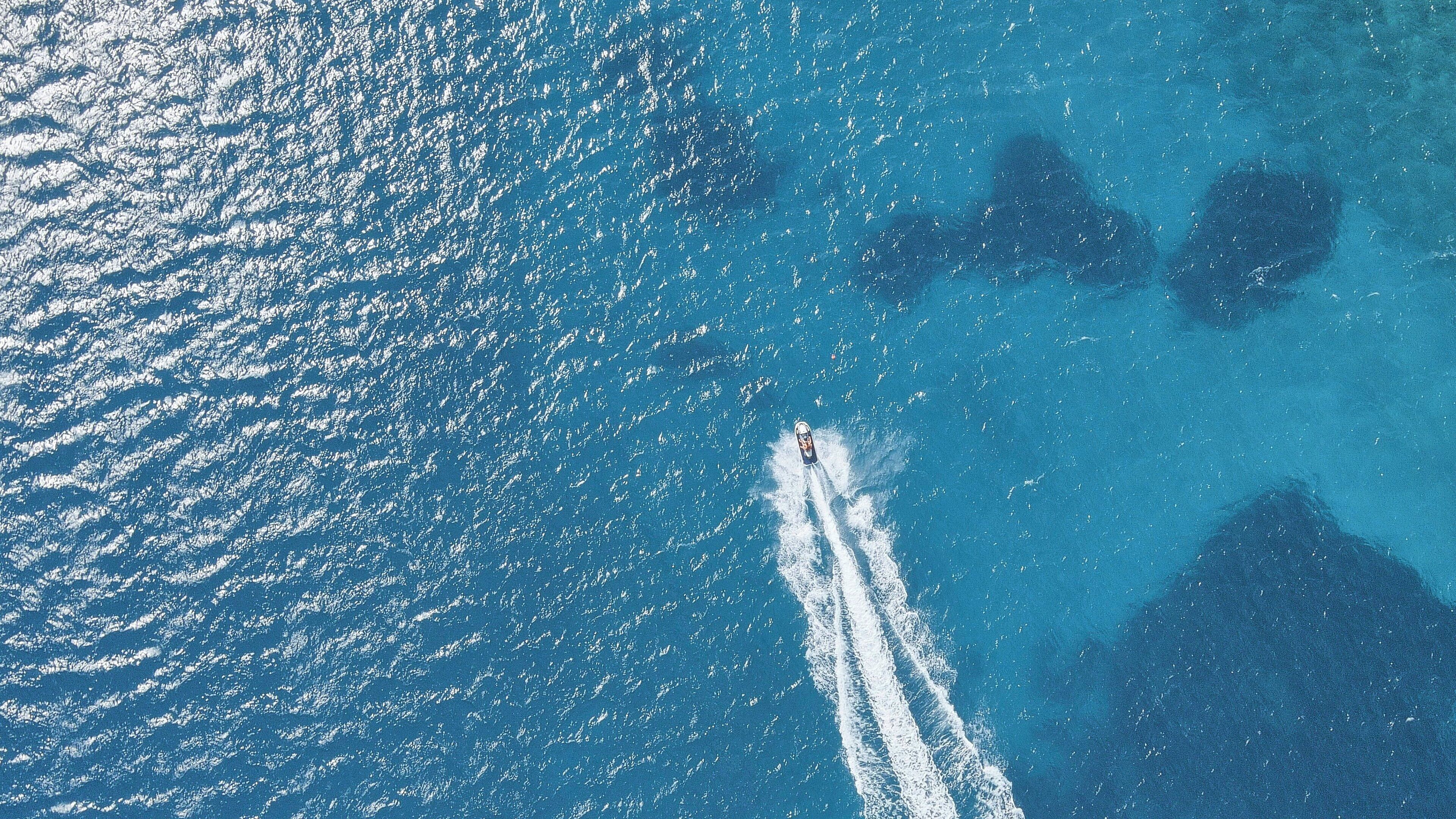Luftaufnahme einer Küstenregion mit klarem, blauem Wasser und einem Boot, das eine Bugwelle hinterlässt.