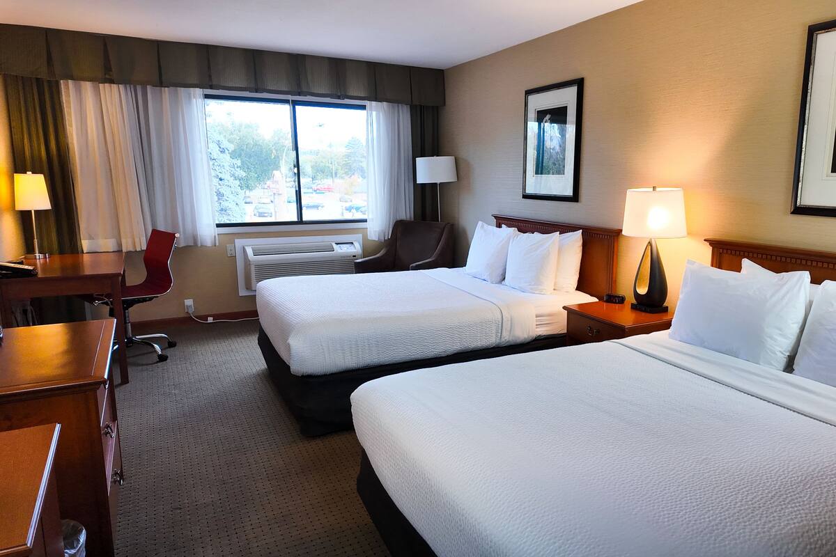 A hotel room with two beds, a desk, a chair, a lamp, and a window with curtains.