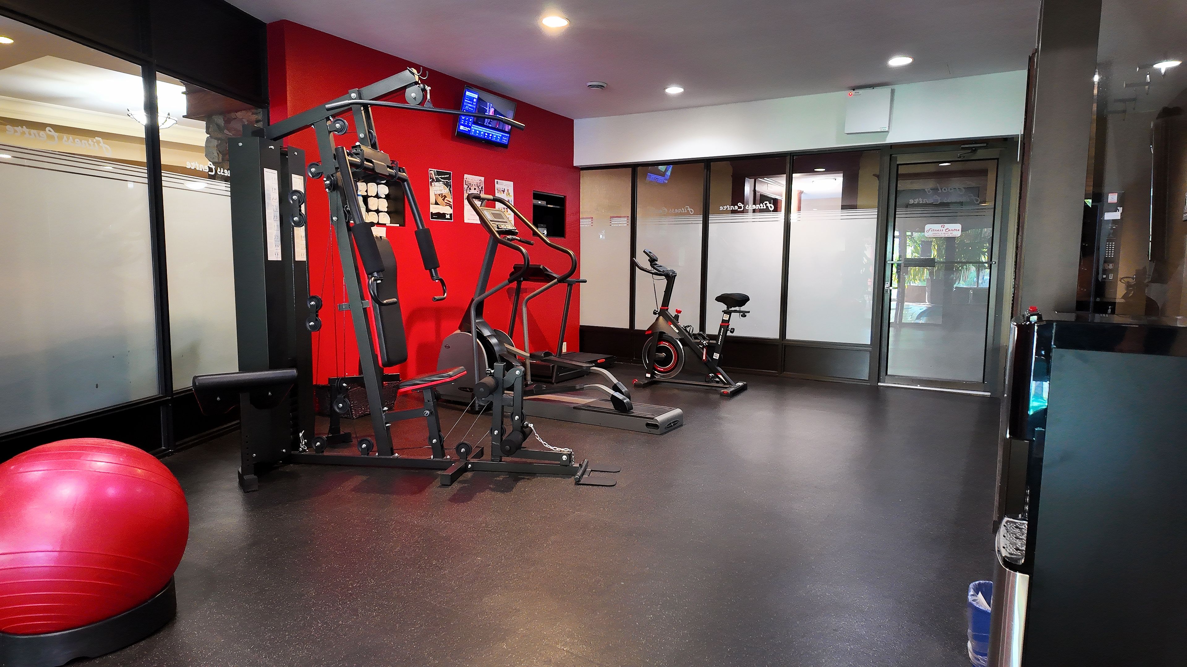 Une salle de sport équipée de matériel d’exercice, avec un mur rouge et une grande fenêtre.