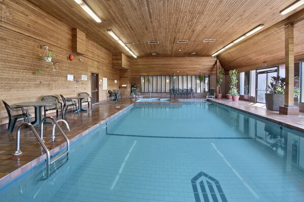 An indoor swimming pool with wooden walls, metal pool ladders, and potted plants. - Ramada Hotel & Conference Center by Wyndham Kelowna (Kelowna)