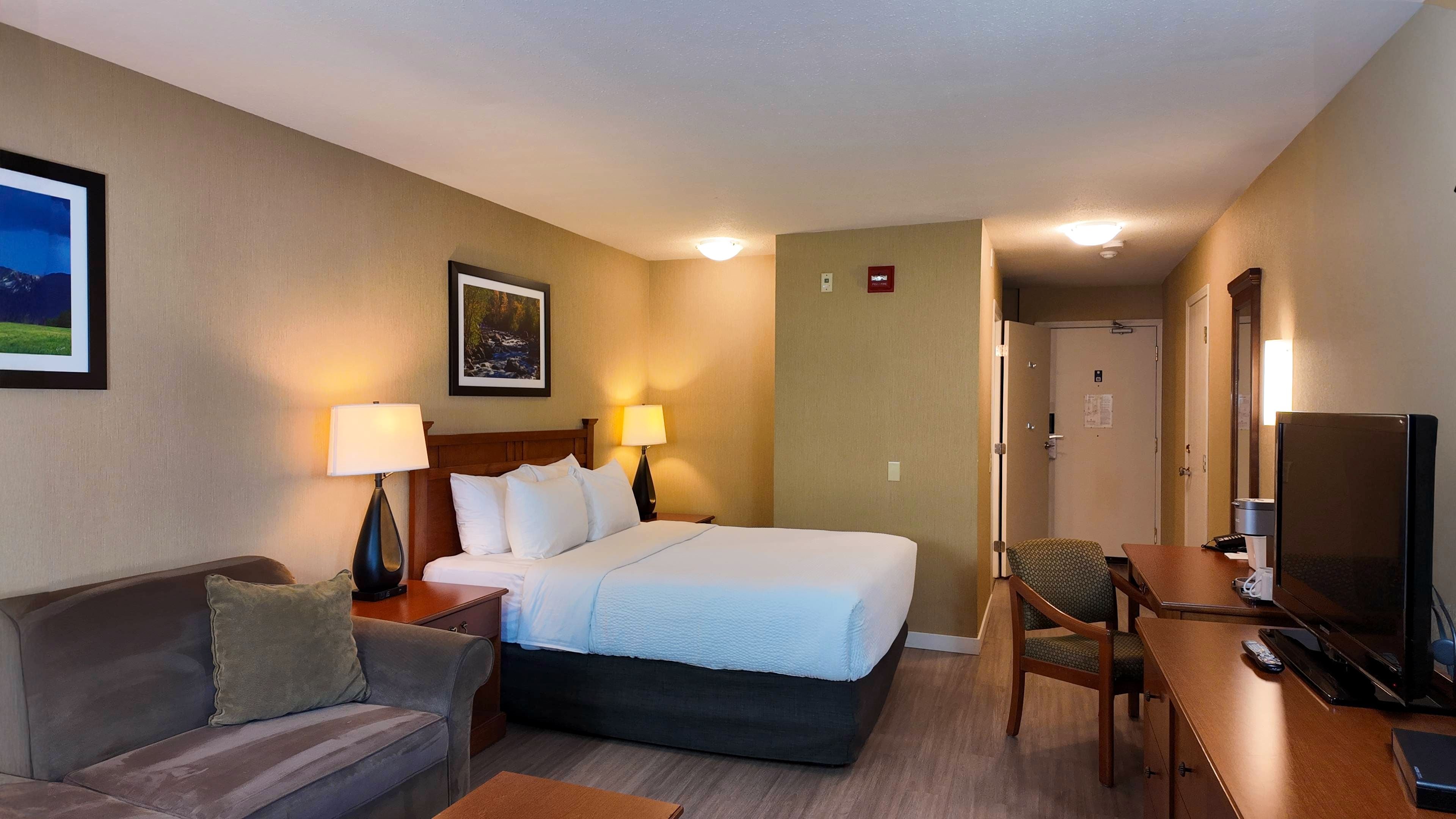 A hotel room with a bed, bedside lamps, a TV, a desk, and a chair.