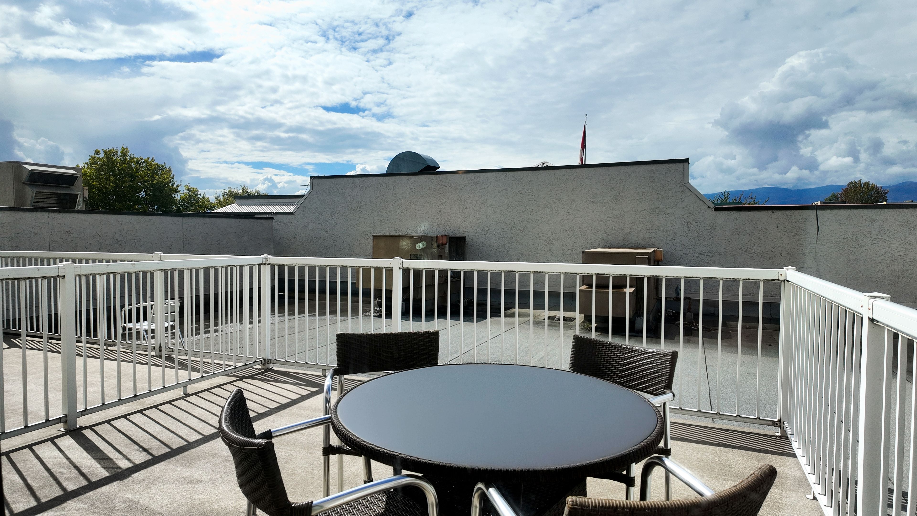 Una terraza en la azotea con una mesa redonda y sillas, rodeada por una barandilla de metal blanco.
