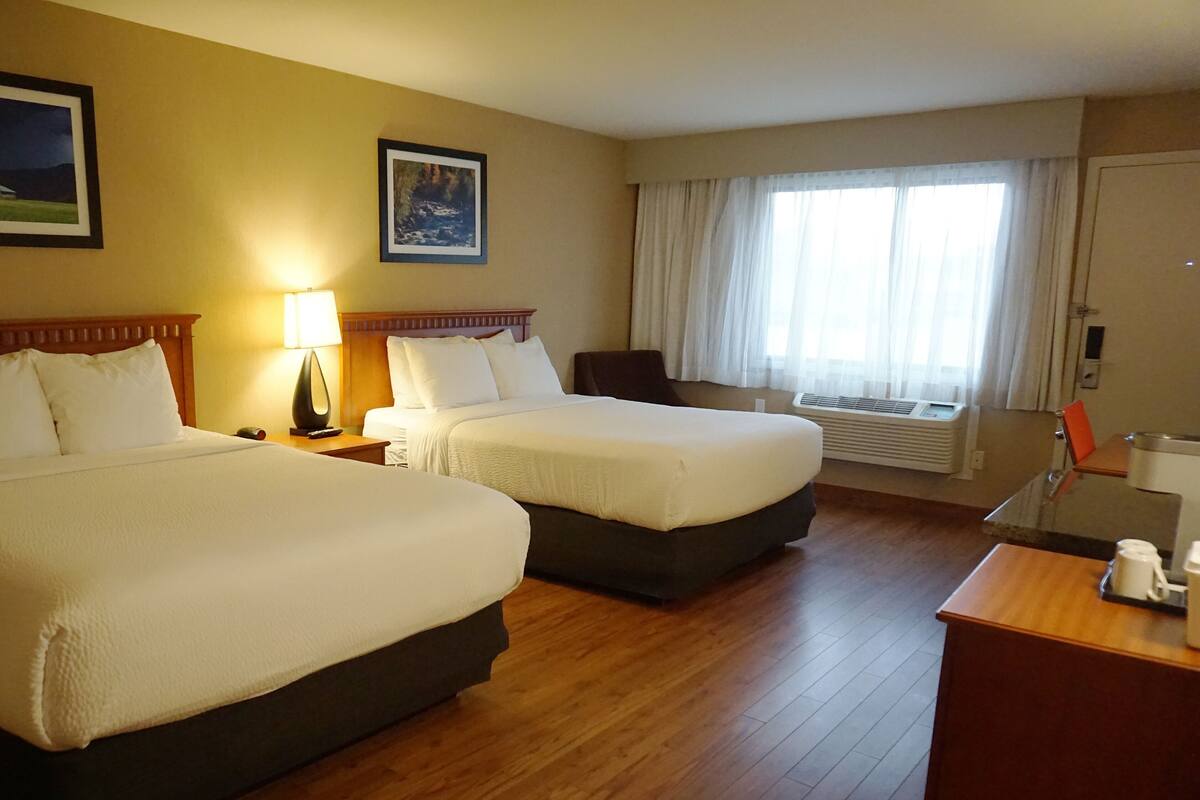 A hotel room with two beds, a desk, a chair, a lamp, and a window with curtains.