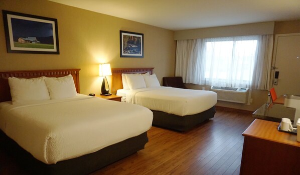 A hotel room with two beds, a desk, a chair, a lamp, and a window with curtains.