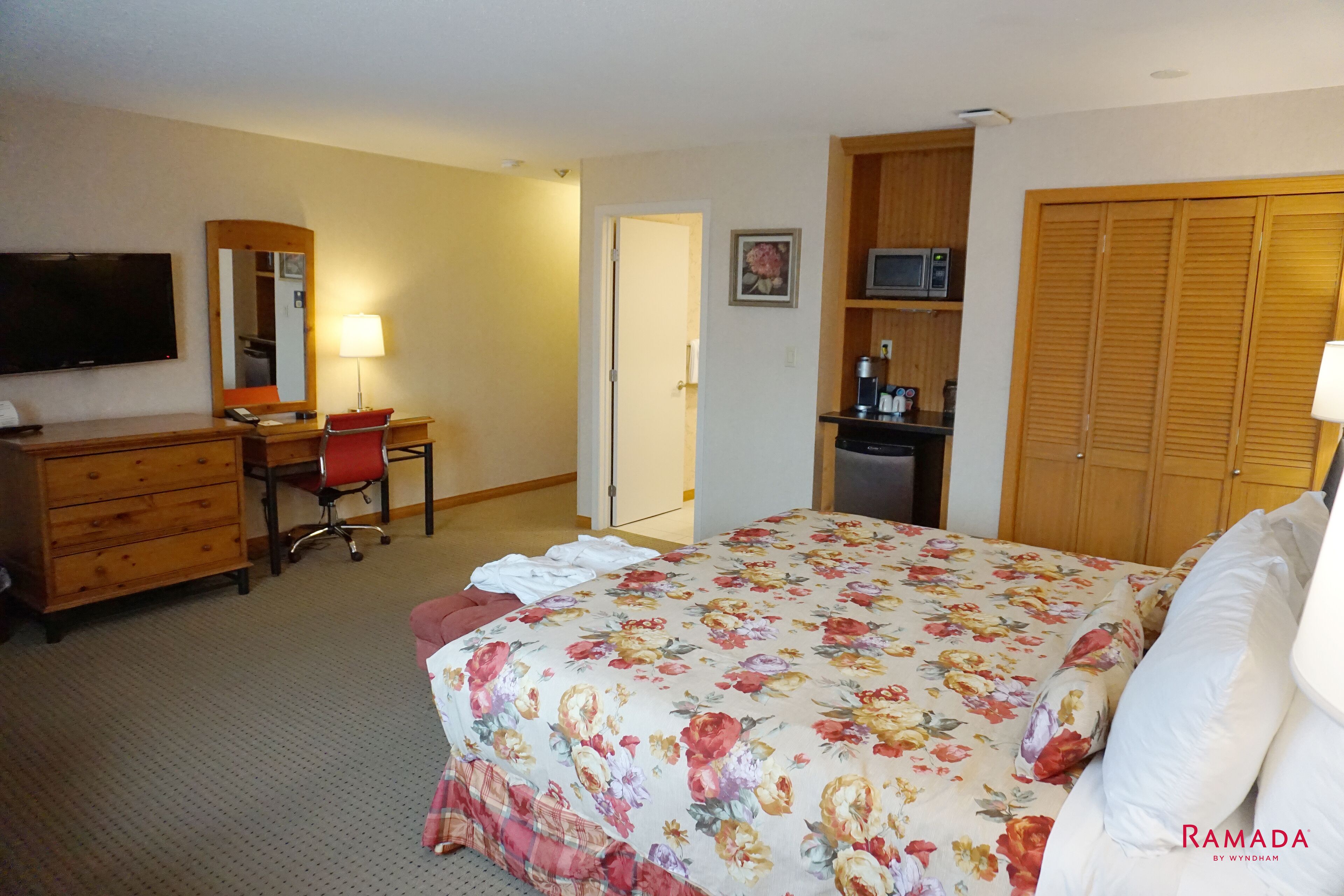 A hotel room with a bed, a desk, a chair, a dresser, a television, a microwave, and a closet.