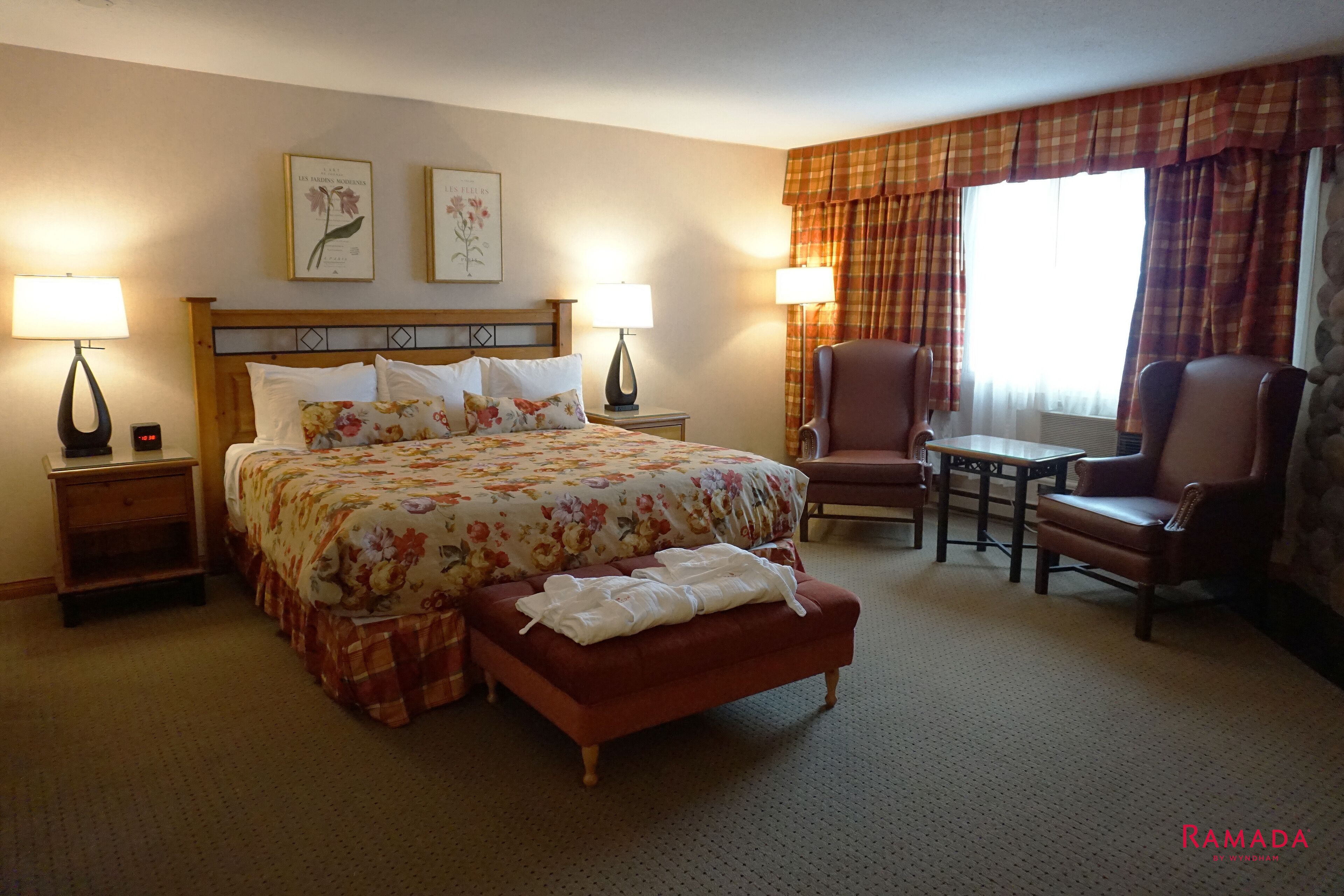 Habitación de hotel con cama, dos mesitas de noche, una silla, una mesita pequeña y una ventana con cortinas.