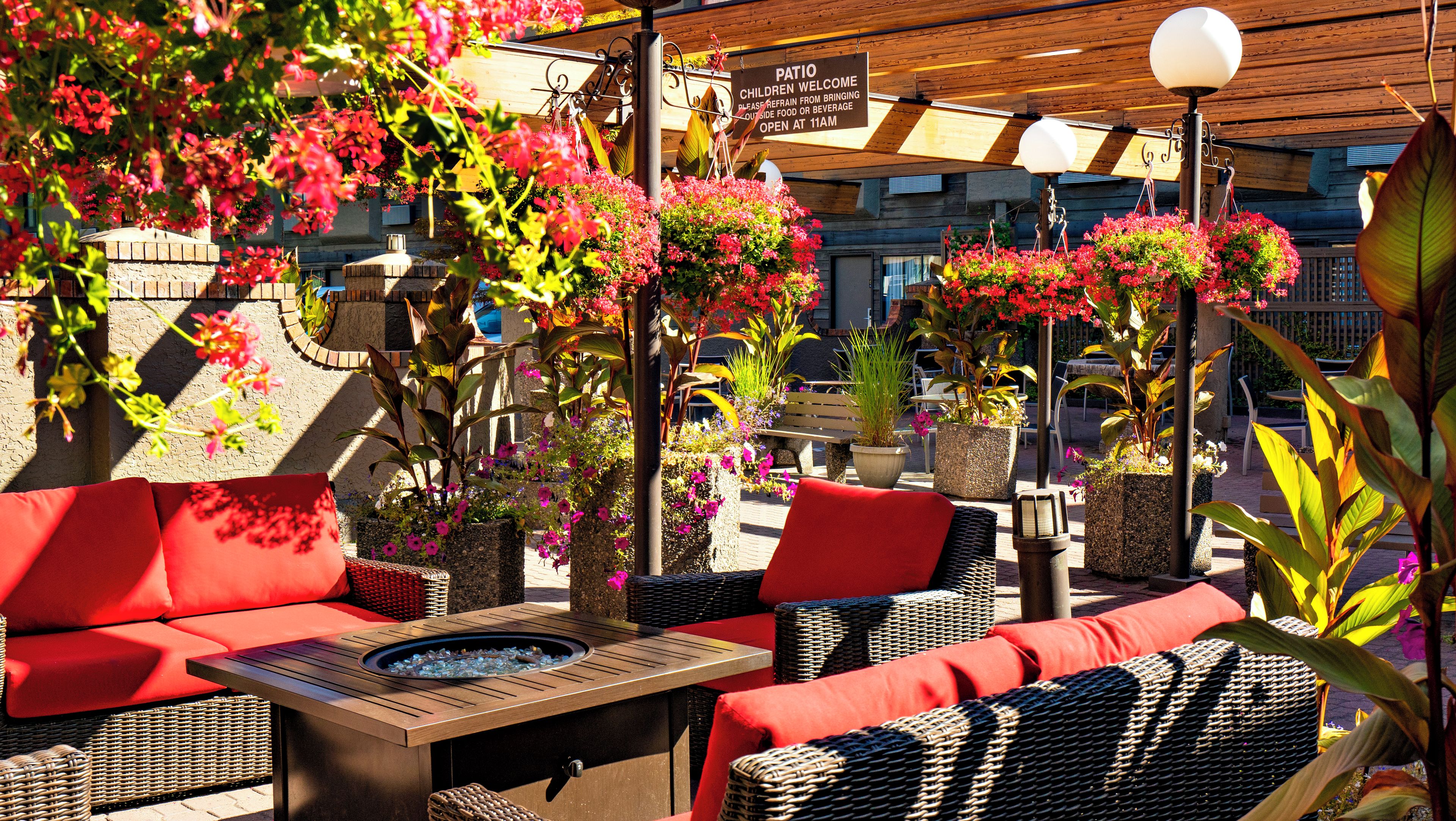 Un espace extérieur aménagé en terrasse, avec des meubles en osier, un foyer et des jardinières suspendues.