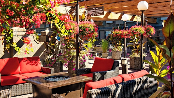 Un espace extérieur aménagé en terrasse, avec des meubles en osier, un foyer et des jardinières suspendues.