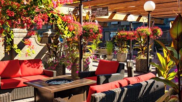 Un patio al aire libre con mobiliario de mimbre, un brasero y macetas colgantes de flores.