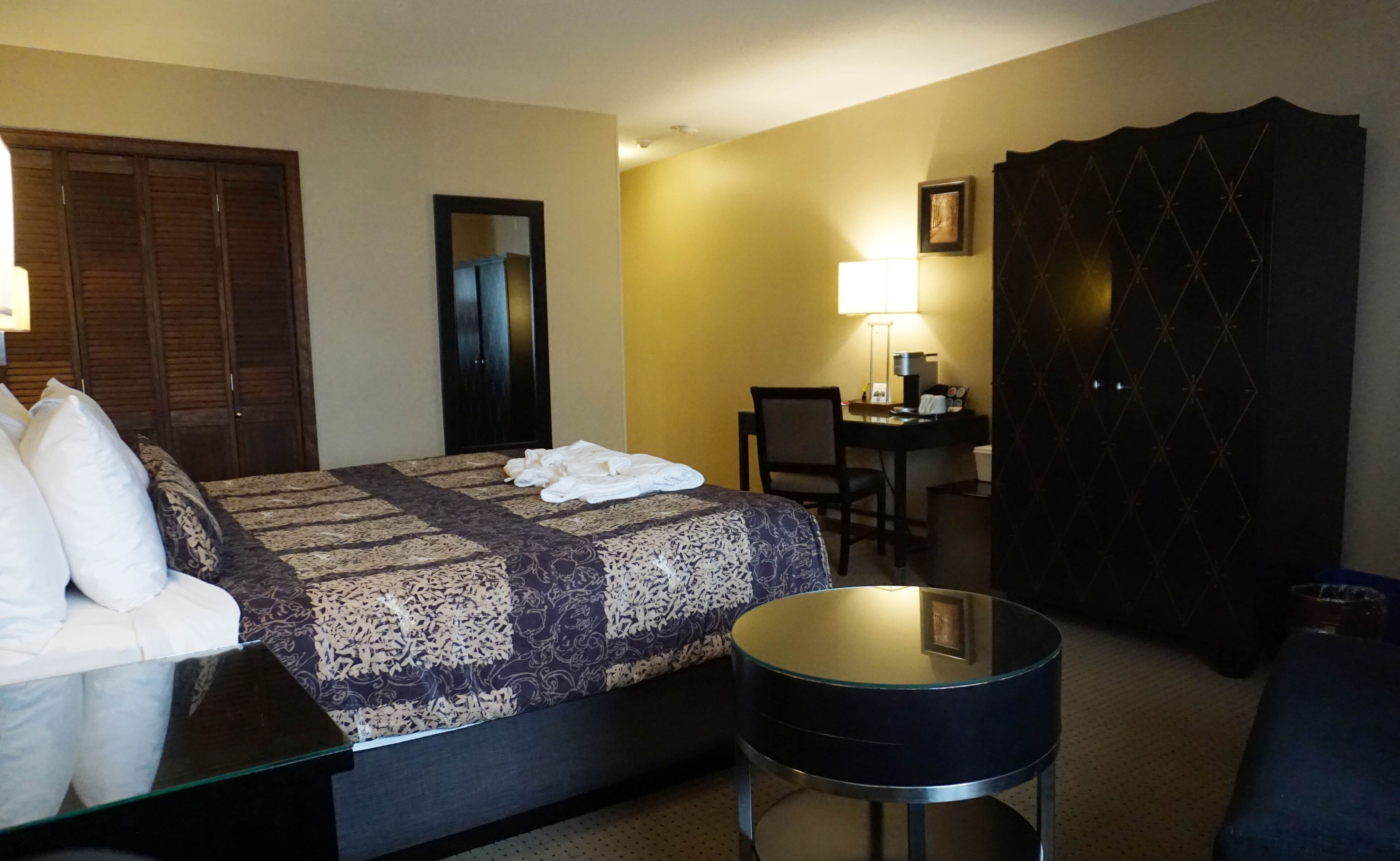 Una camera d'albergo con un letto, una scrivania, una sedia, un tavolino rotondo e un armadio.