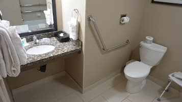 Um banheiro com pia de bancada de granito, vaso sanitário branco, corrimão e um quadro pendurado na parede.