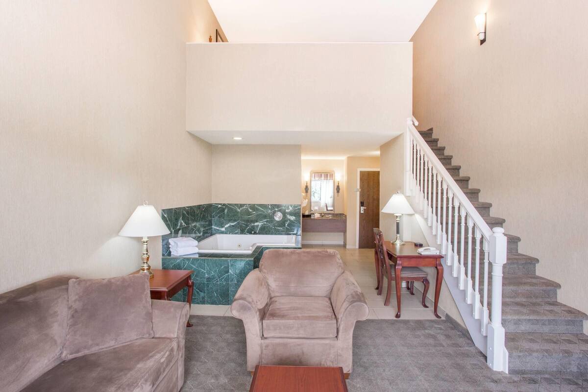 A hotel lobby with a sofa, armchairs, a small table, a lamp, a bathtub, and a staircase.