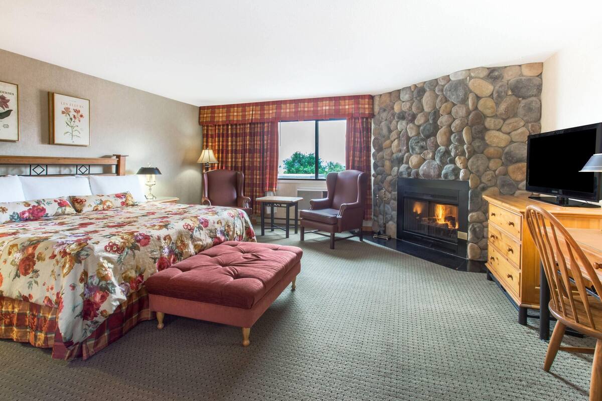 A hotel room with a bed, a fireplace, a TV, and a view of the outdoors.