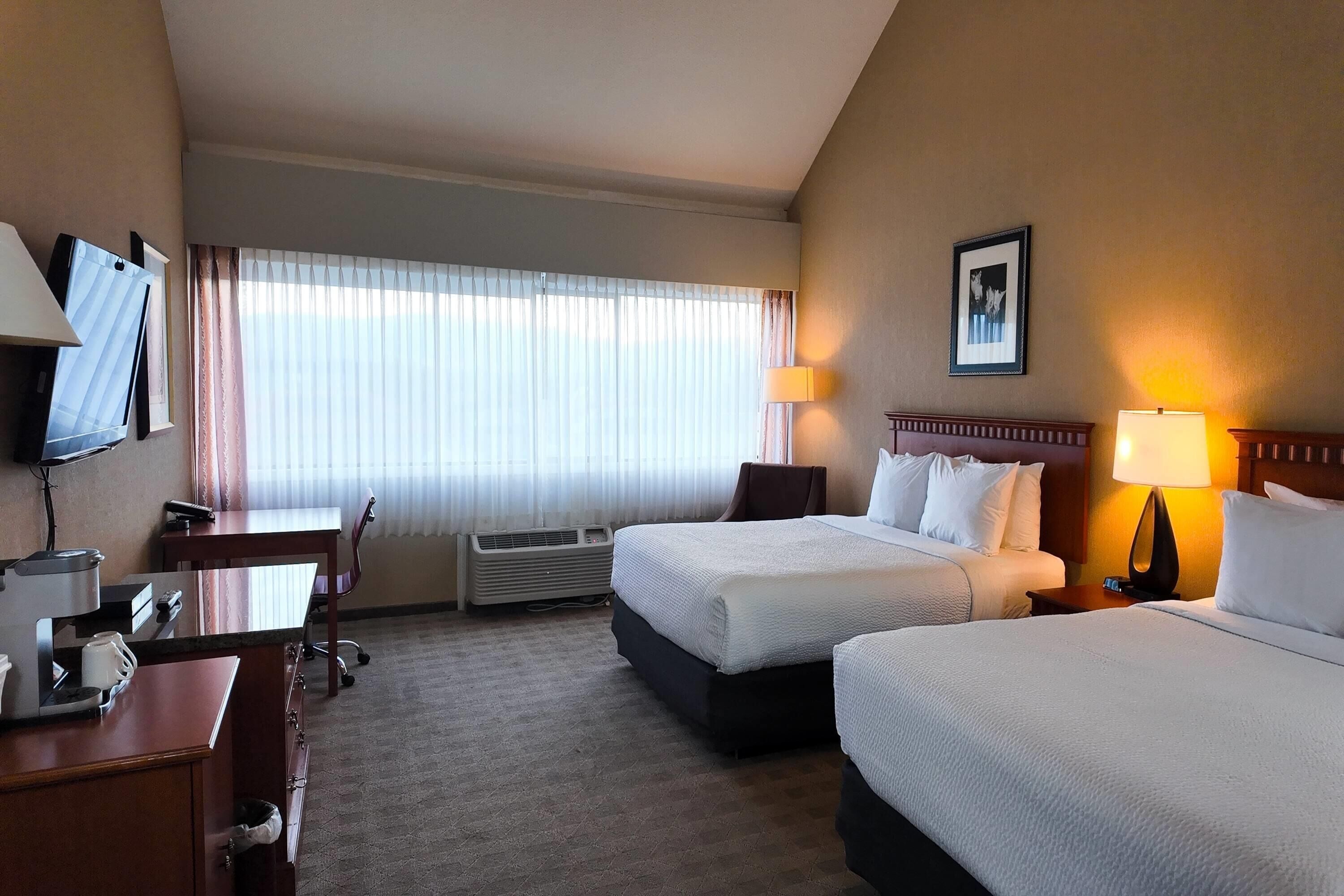 Habitación de hotel con dos camas, un escritorio con silla, un televisor y un cuadro en la pared.