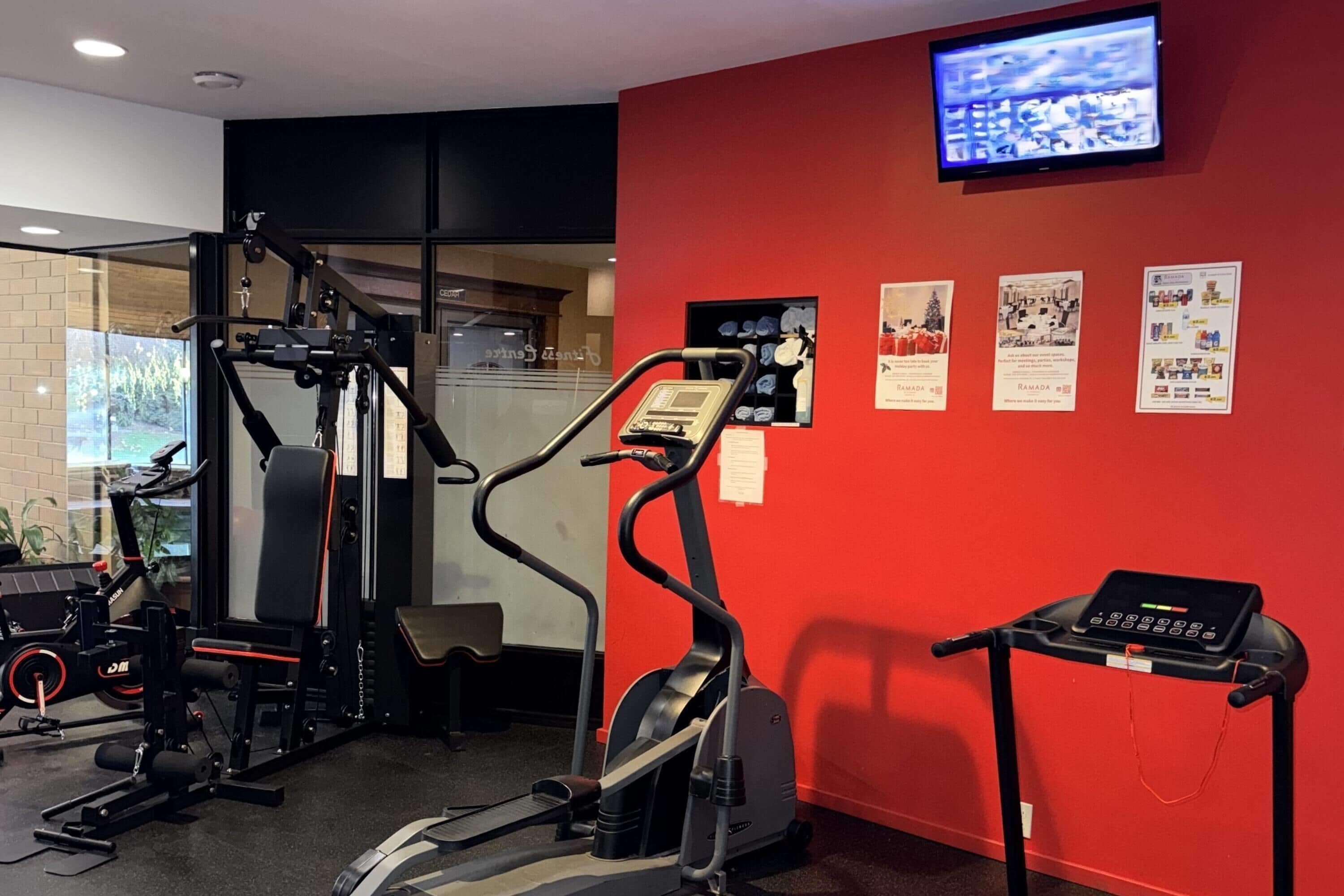Un gimnasio con equipamiento de ejercicio, un televisor en la pared y carteles informativos.