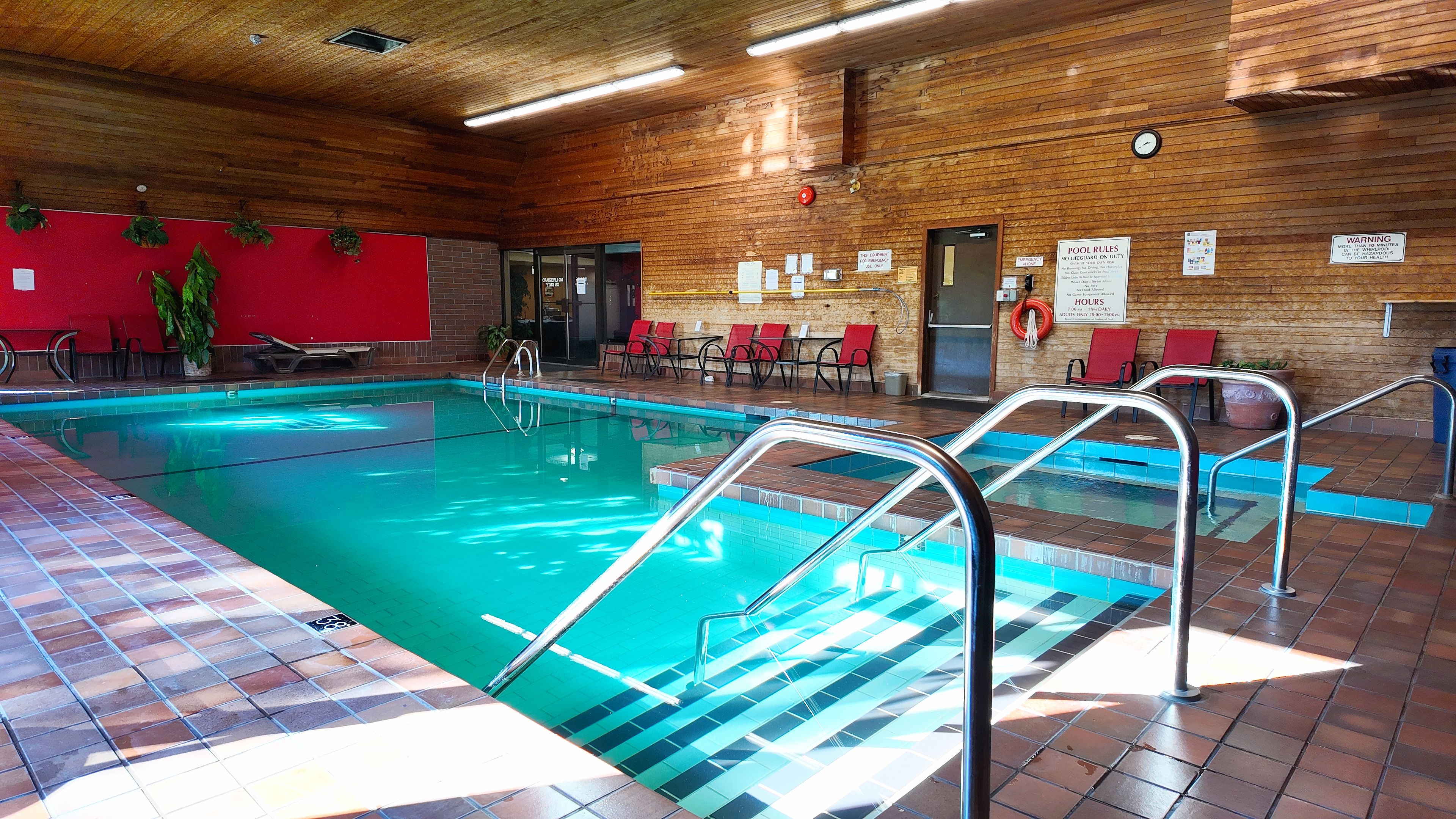 Una piscina interior con suelo de baldosas, escaleras metálicas y una pared de madera con varios carteles.