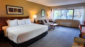 A hotel room with a large bed, a sofa, a small table, and a window with a view of trees.