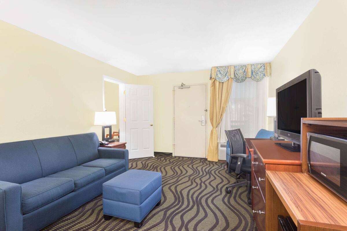 A hotel room with a blue sofa, an ottoman, a television, and a desk with a computer.