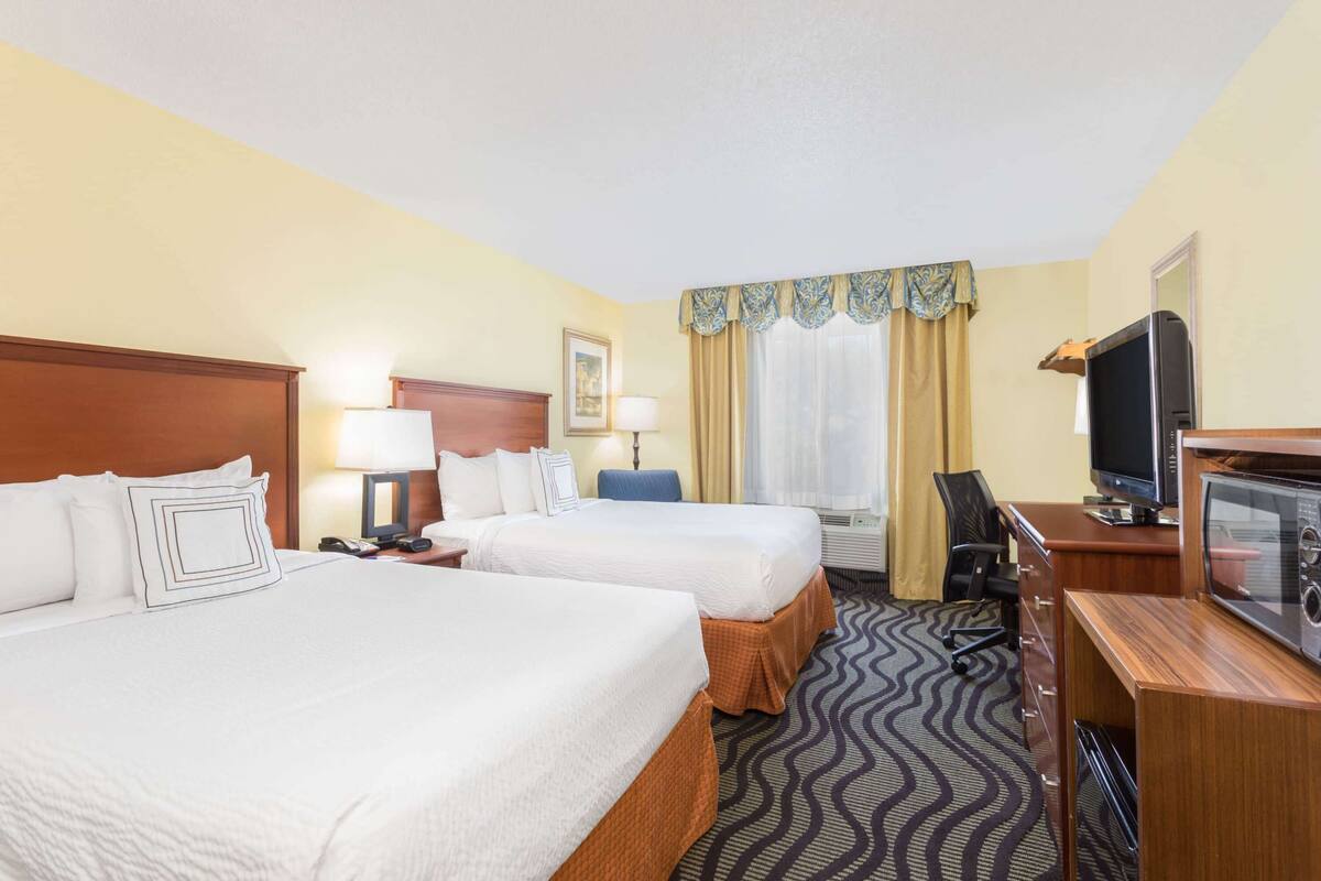A hotel room with two beds, a desk with a television, a chair, and a desk lamp.