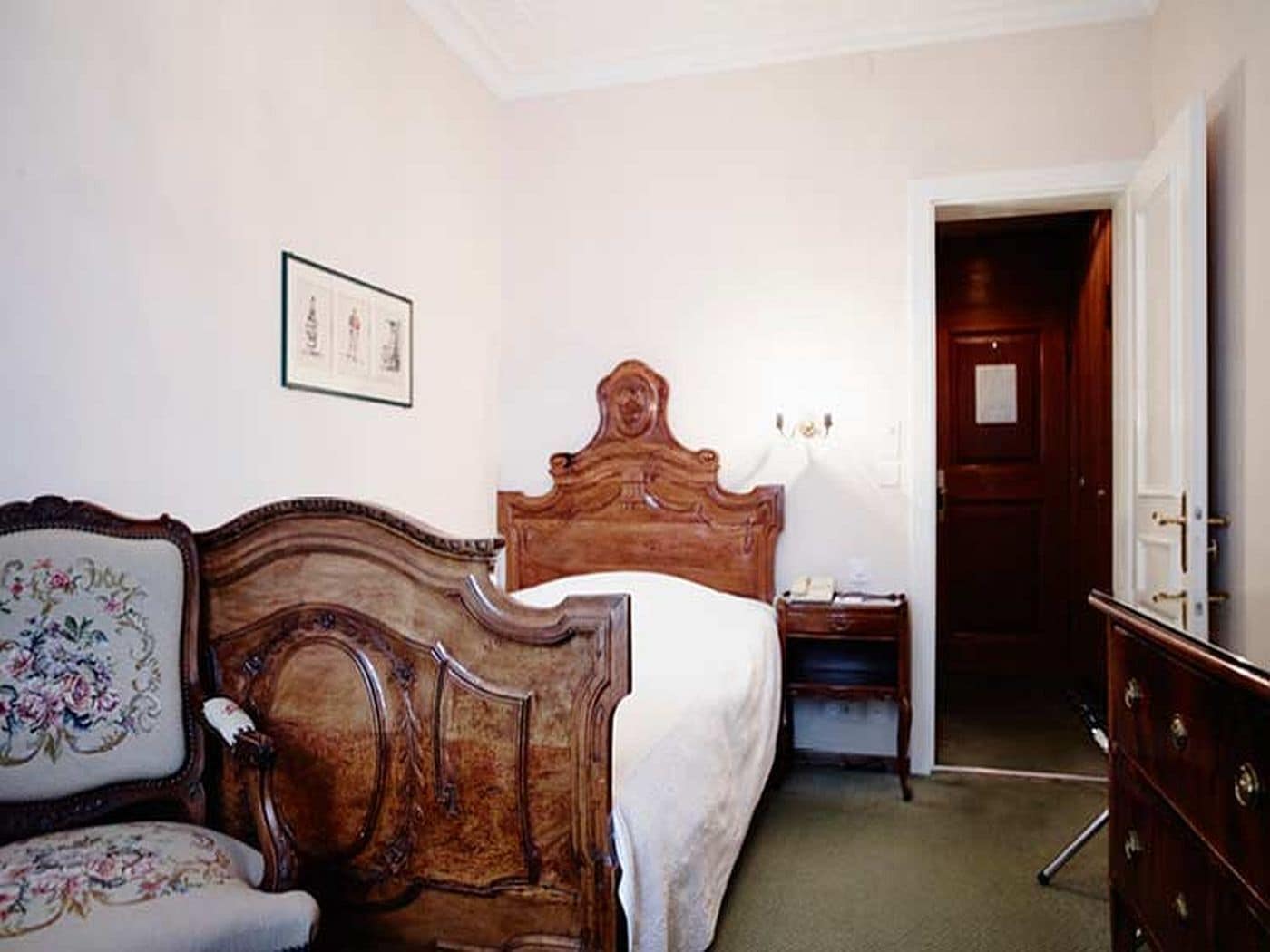 A bedroom with a wooden bed, a nightstand, a dresser, and a door leading to another room.