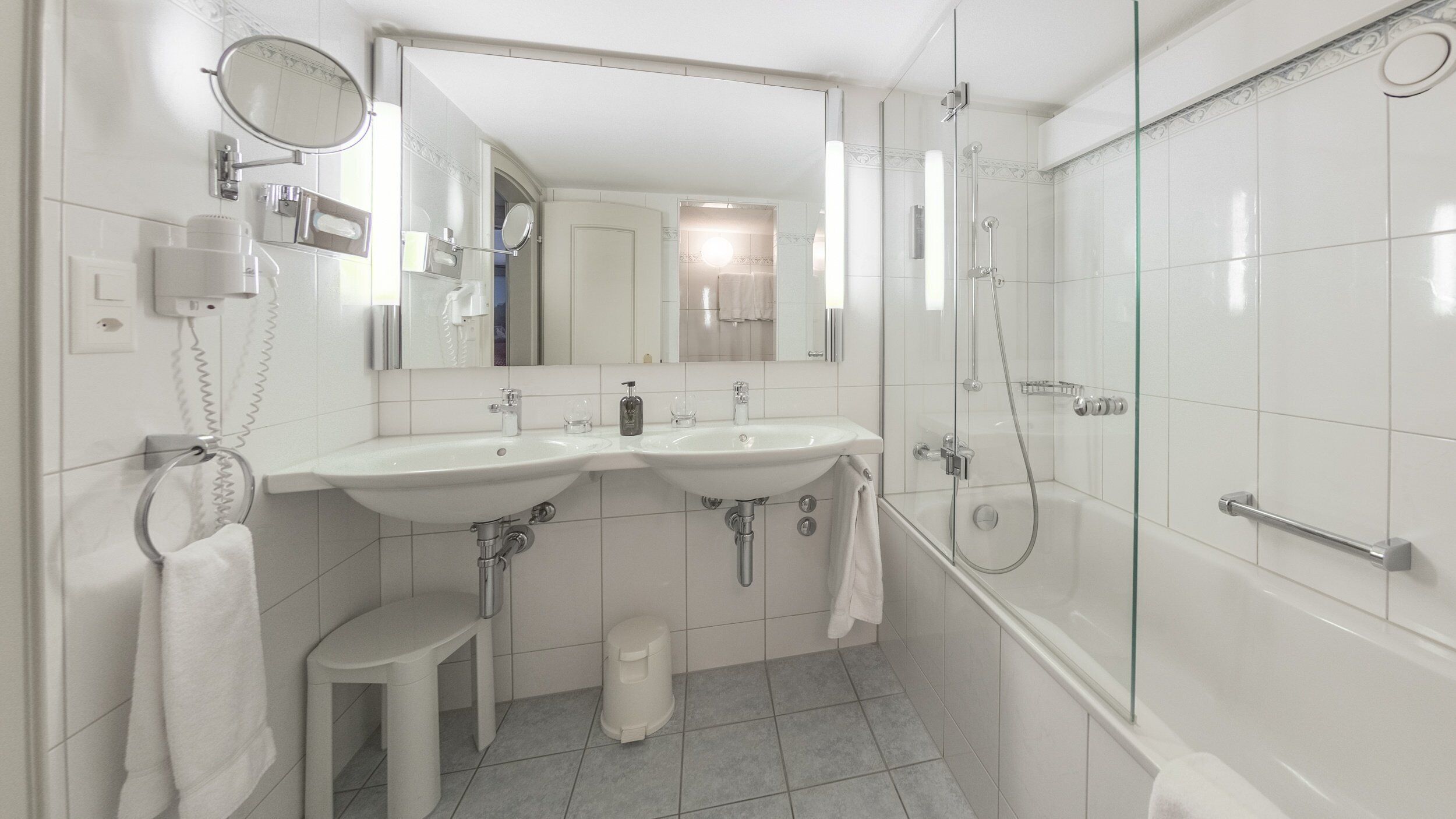 A modern bathroom with two sinks, a mirror, a toilet, and a glass-enclosed shower.