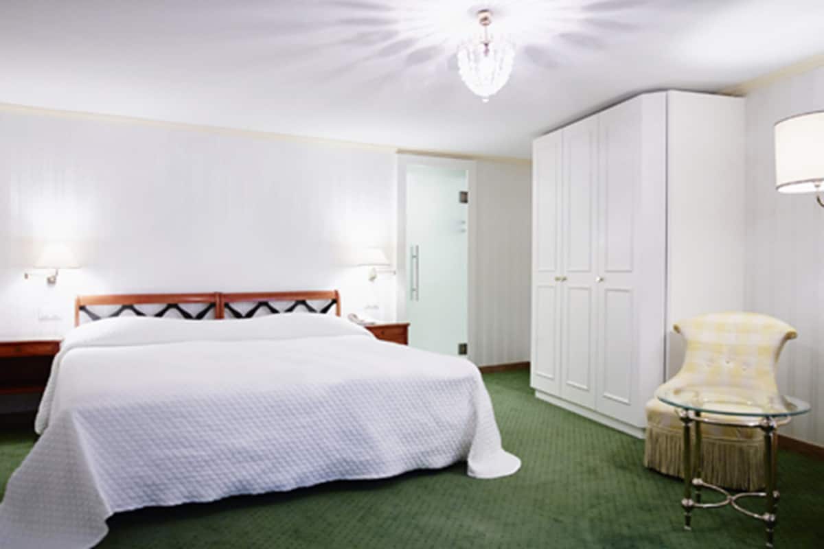 A hotel room with a bed, a wardrobe, a chair, and a lamp.