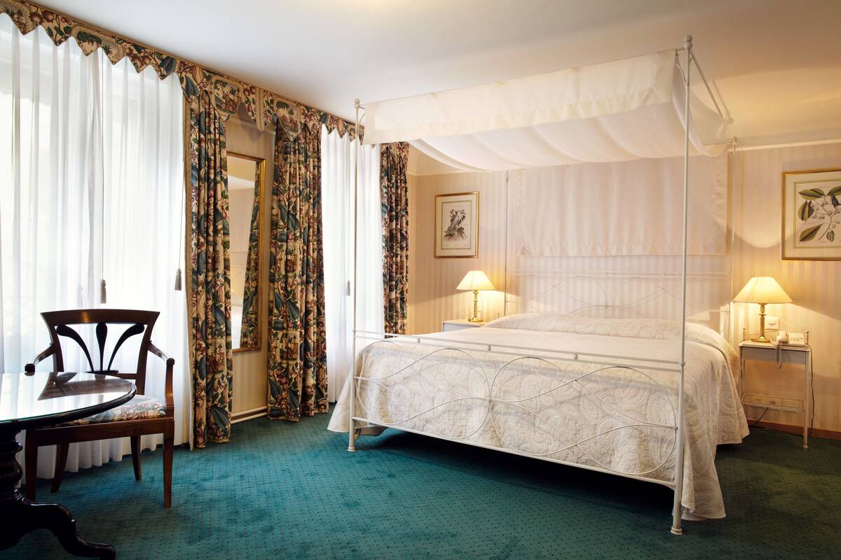 A four-poster bed with a canopy, a wooden chair, a small table, and two bedside lamps.
