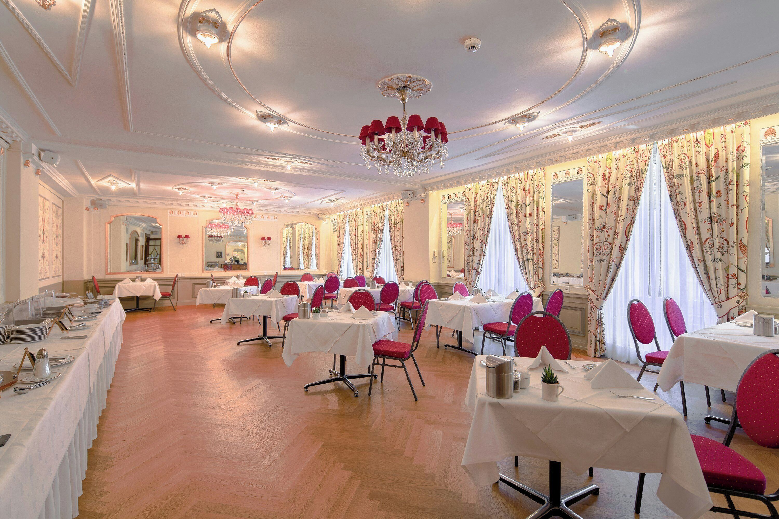 A formal dining room with white tables, red chairs, and a chandelier.