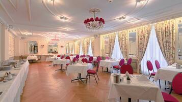 A formal dining room with white tables, red chairs, and a chandelier.
