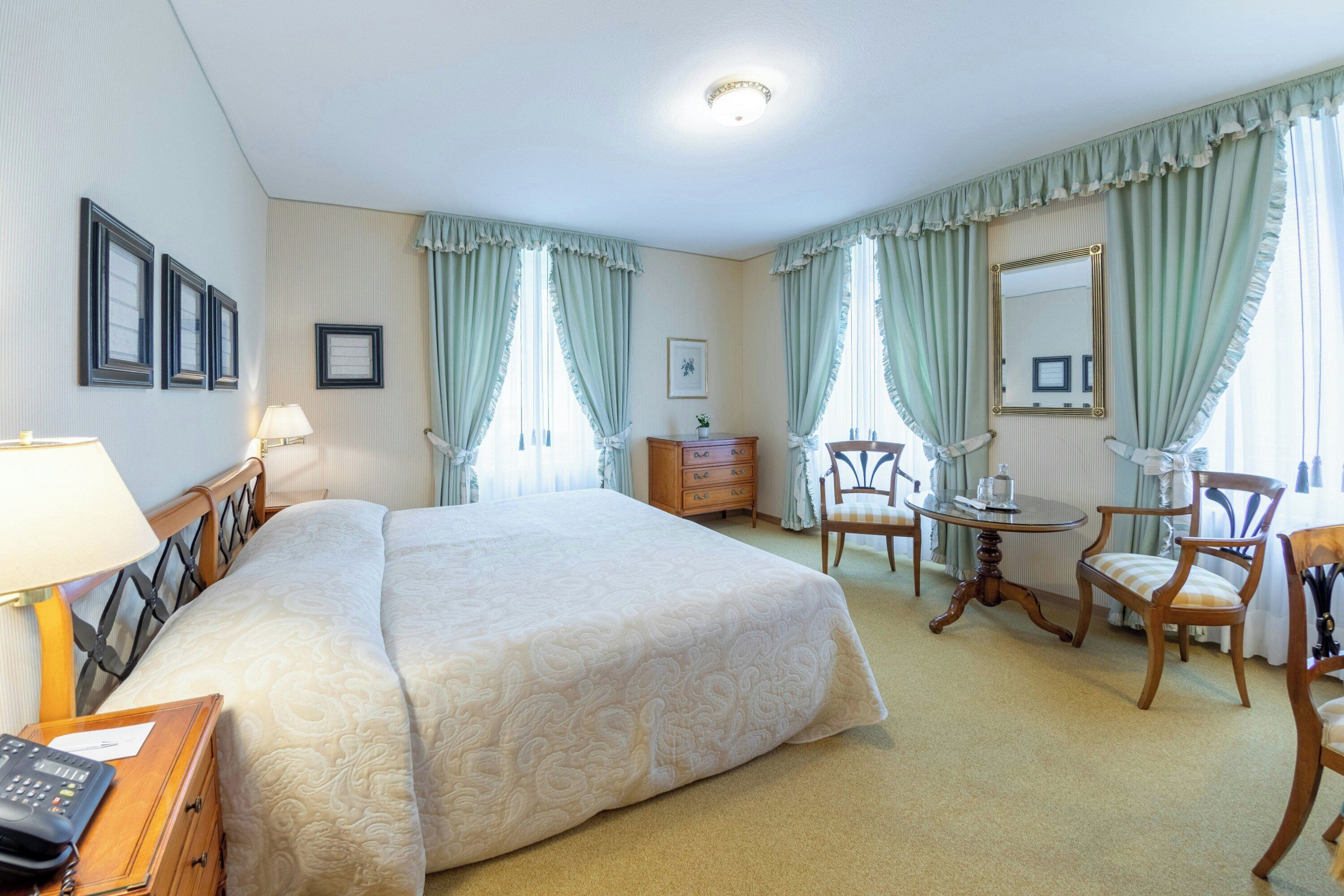 Habitación de hotel con una cama grande, un escritorio, una silla, una mesita y un espejo.