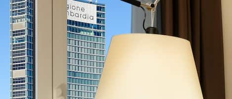 Egy szoba, melynek ablakán át egy magas épület látható, és az épületen a „Regione Lombardia” felirat olvasható.