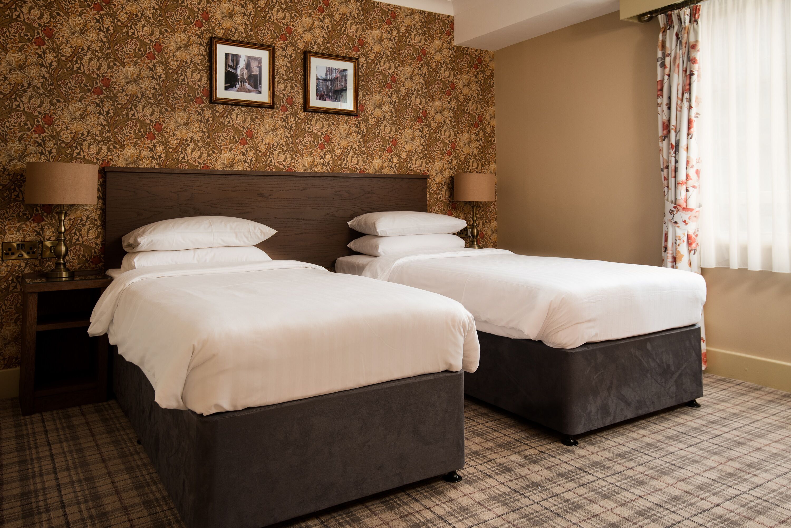 A hotel room with two beds, a floral wallpaper, and a checkered floor.