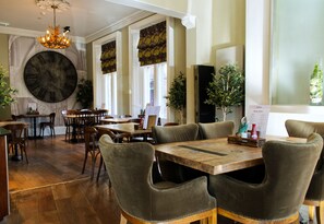 A spacious dining area with wooden tables and chairs, a large wall clock, and decorative plants. - Dean Court Hotel (York)