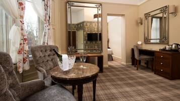 A hotel room with a large mirror, a round table with two wine glasses, a sofa, a desk with a chair, and a dresser.