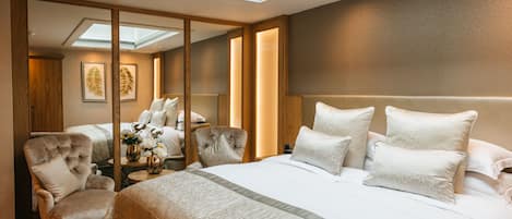 A modern hotel room with a large bed, a sitting area with a chair, a small table with a vase of flowers, and a skylight above the bed.