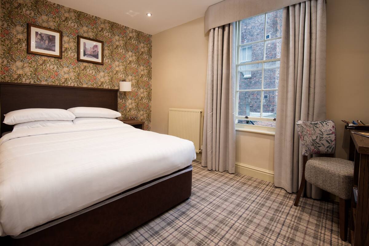 Une chambre d’hôtel avec un grand lit, une chaise, une fenêtre avec des rideaux et un radiateur.