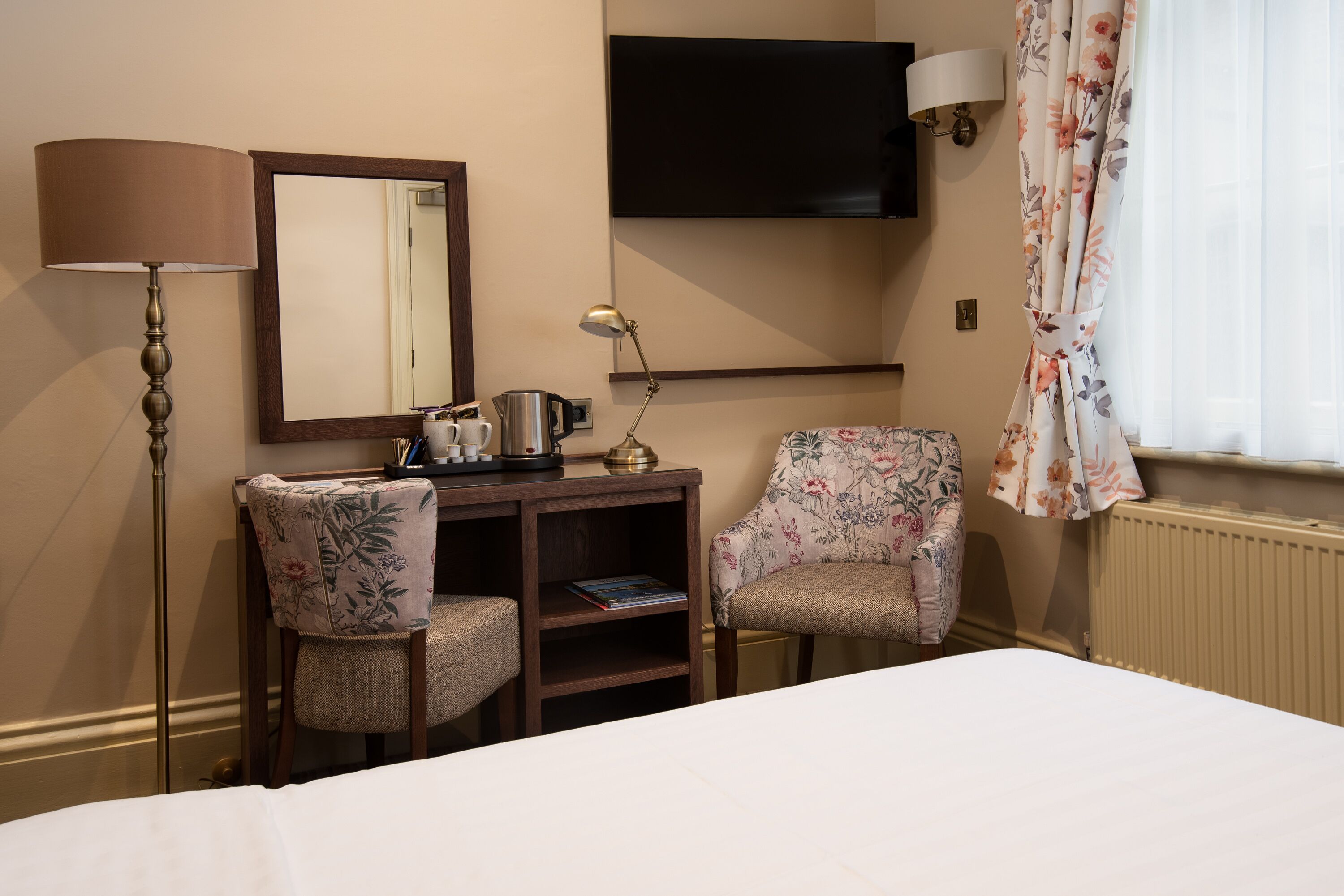 Una habitación de hotel con una cama, un escritorio con lámpara, una silla, un televisor y una ventana con cortinas.