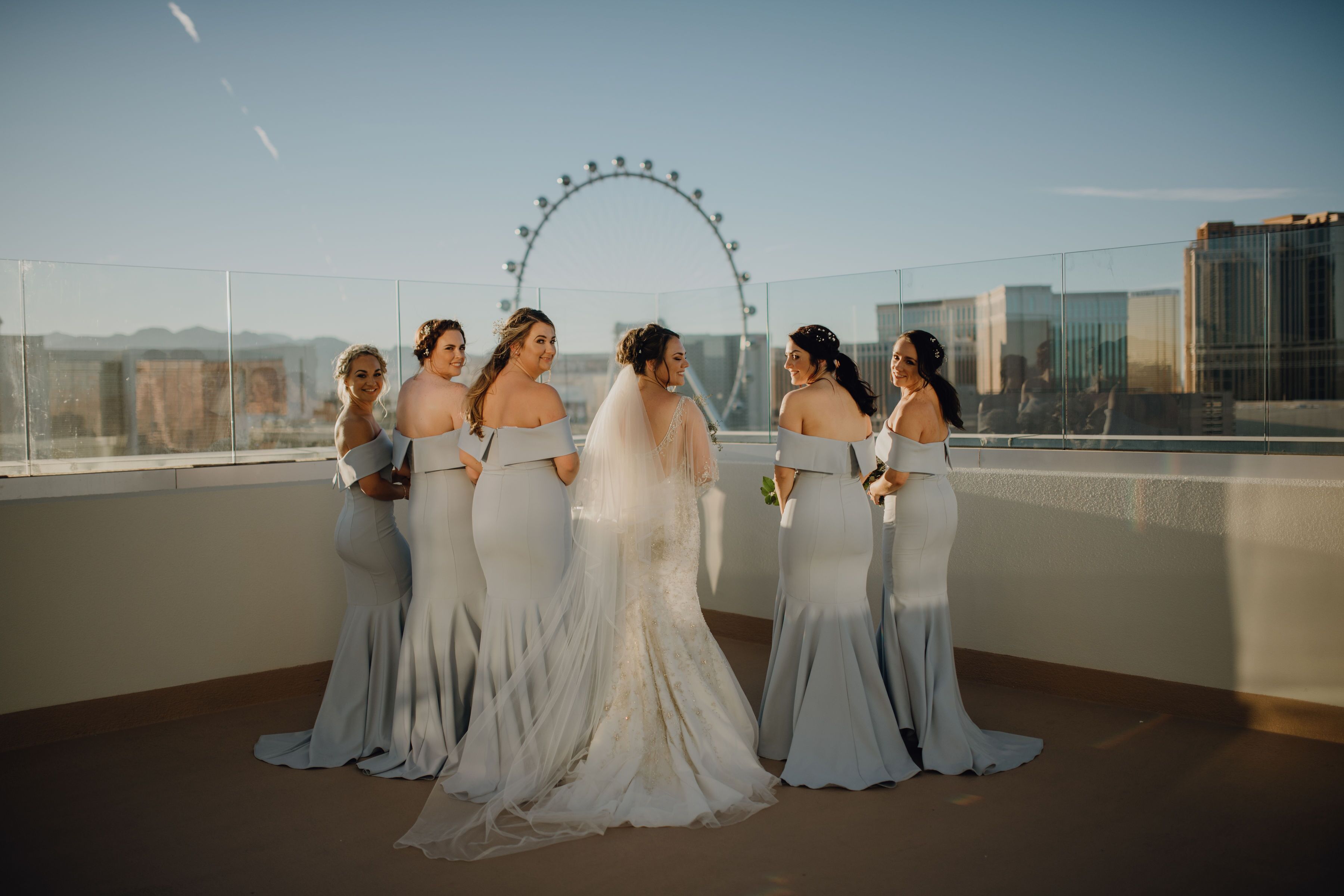 A group of women in wedding dresses on a balcony with a cityscape and a Ferris wheel in the background.