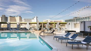 A rooftop pool area with lounge chairs, a Ferris wheel, and city buildings in the background.