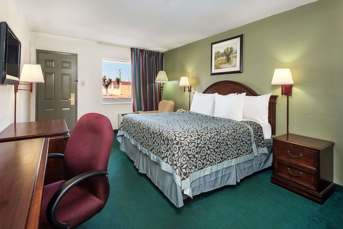 A hotel room with a bed, a desk, a chair, a nightstand, and a lamp.