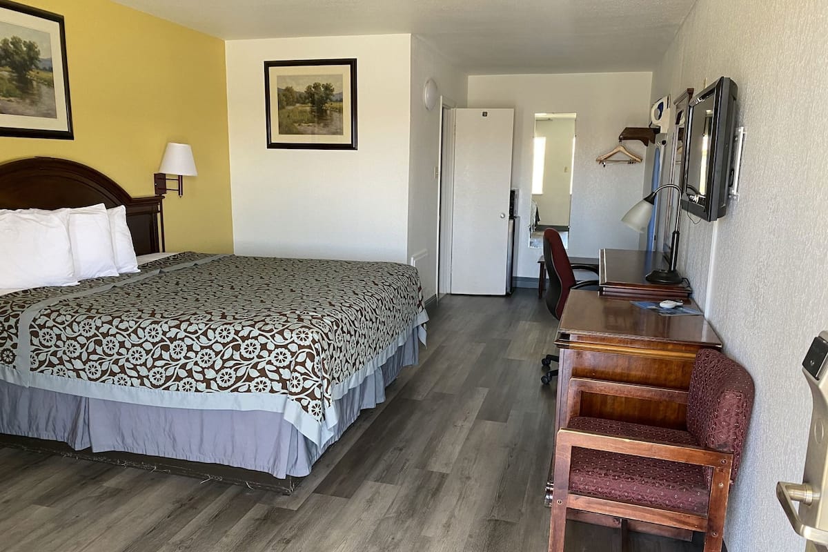 A hotel room with a bed, a desk with a chair, a mirror, and a door leading to a bathroom.